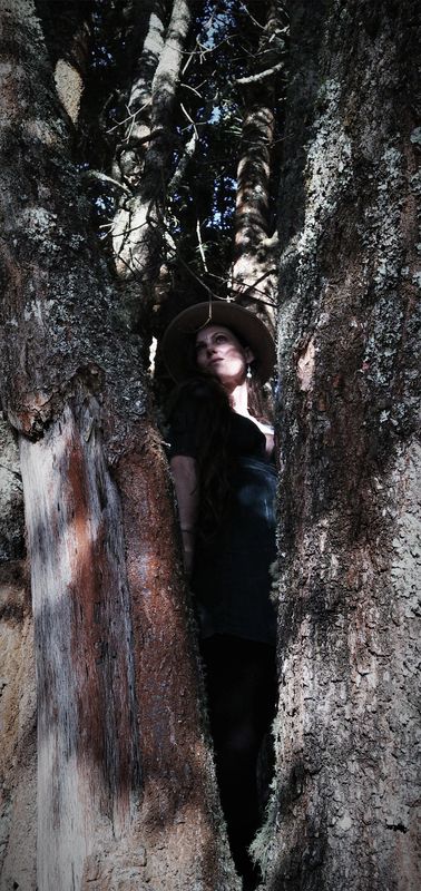 Michela standing between two ancient trees, wearing a hat